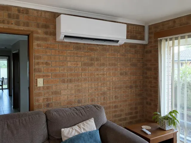 Split system head on a brick wall above a couch, louvre open, in a living room in Para Hills